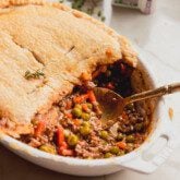 Beef pot pie with a crust and meat filling in a casserole dish with a spoon.