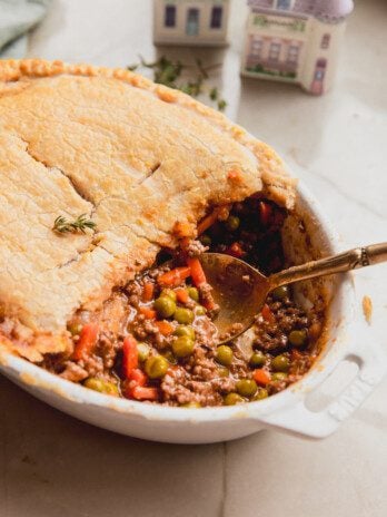 Beef pot pie with a crust and meat filling in a casserole dish with a spoon.