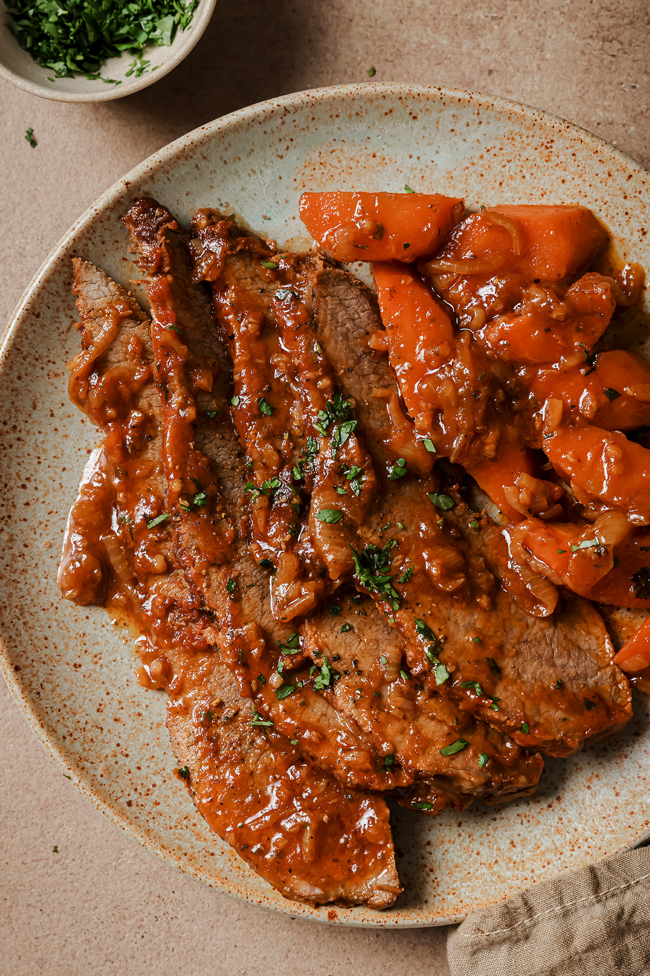 A plate with a serving of sliced brisket with vegetables with it.
