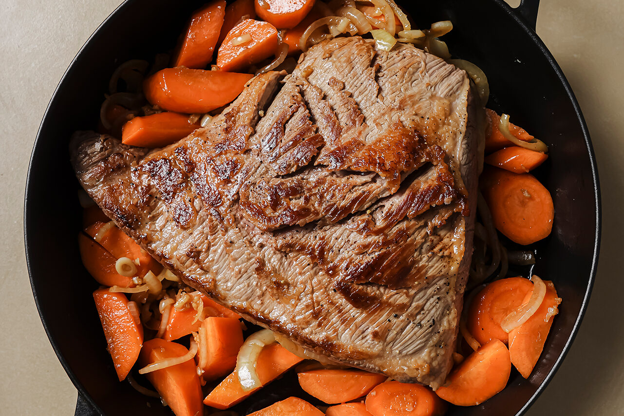 The seared brisket on top of the sauted veggies in the cast iron skillet.