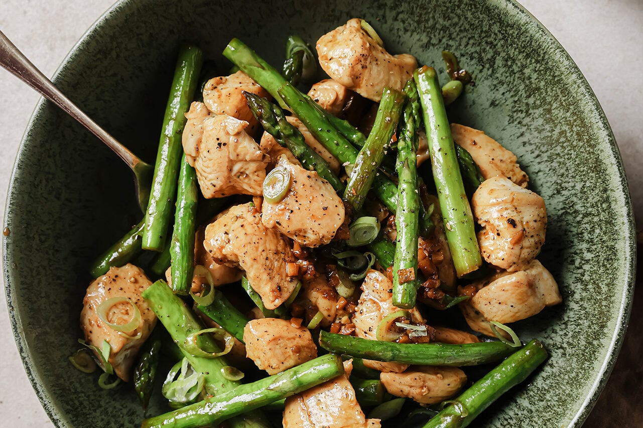 A green bowl filled with lemon & asparagus chicken skillet with a metal fork in it.