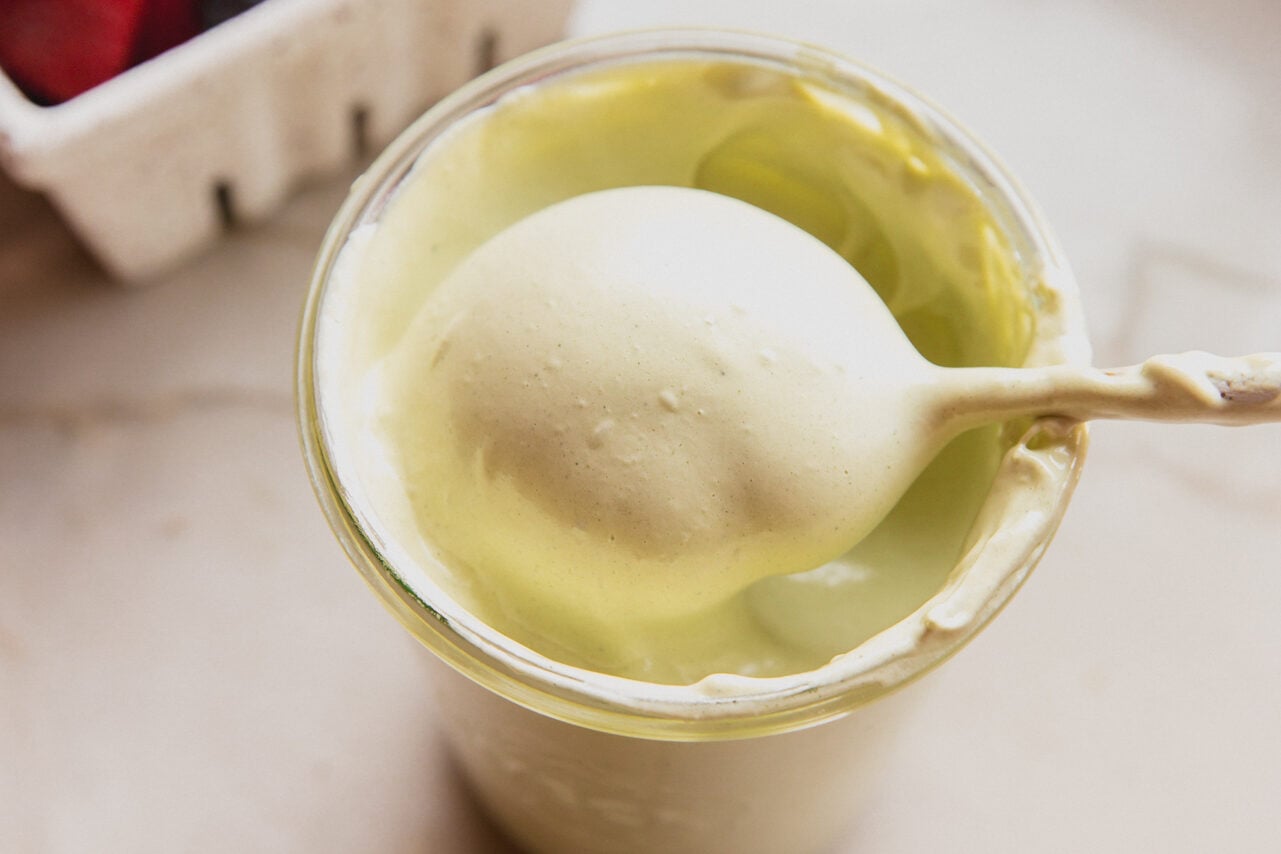 A glass jar of matcha marshmallow fluff with a spoon taking a spoonful out of it.