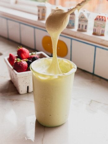 Matcha marshmallow fluff in a jar with a spoon dipping in and pulling up the marshmallow cream.