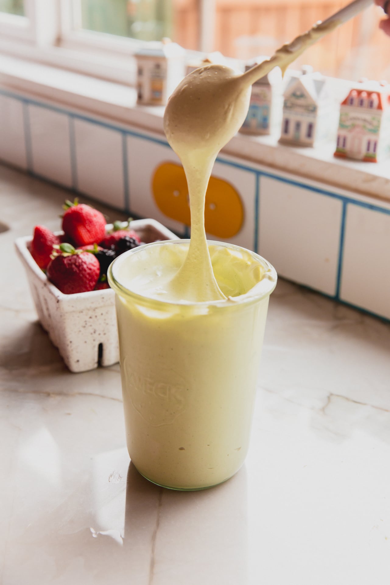 Matcha marshmallow fluff in a jar with a spoon dipping in and pulling up the marshmallow cream.