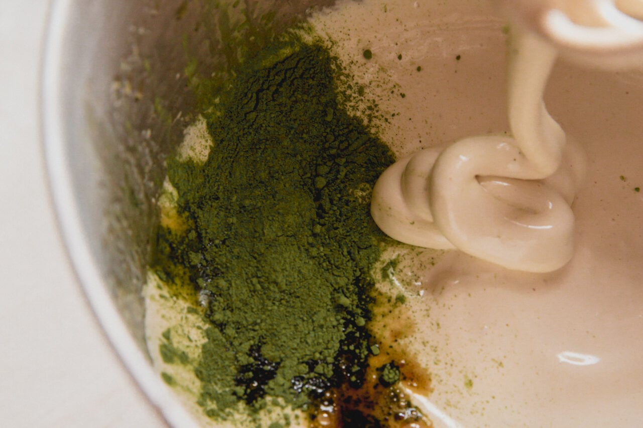 A stand mixer with the honey water gelatin mixture after whipping having vanilla and matcha added in.