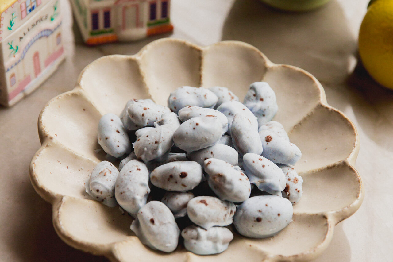 Blue chocolate covered almonds with brown speckles in a bowl with spring kitchen decor in the background.