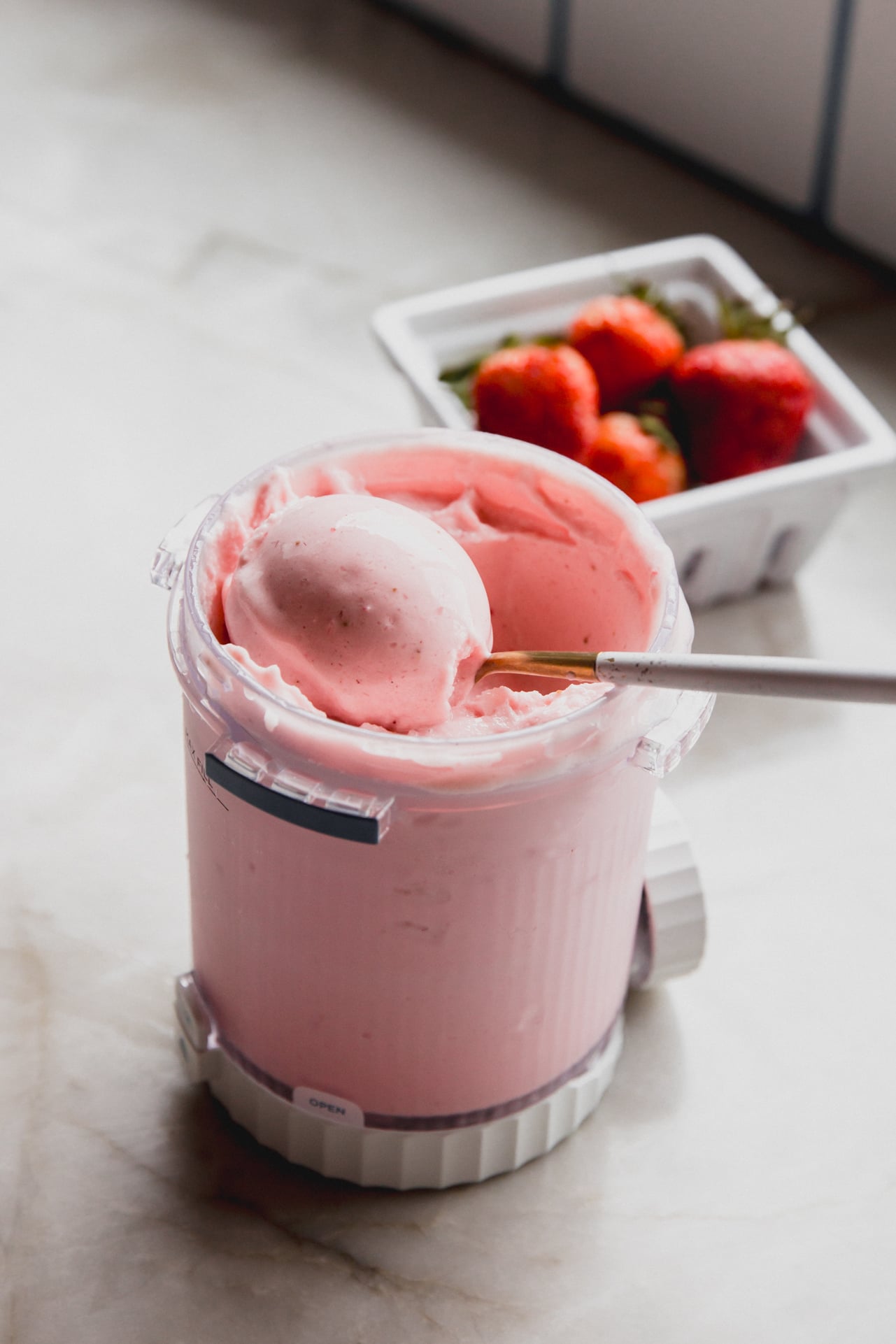 Ninja creami strawberry ice cream in a plastic container, being scooped with a spoon.