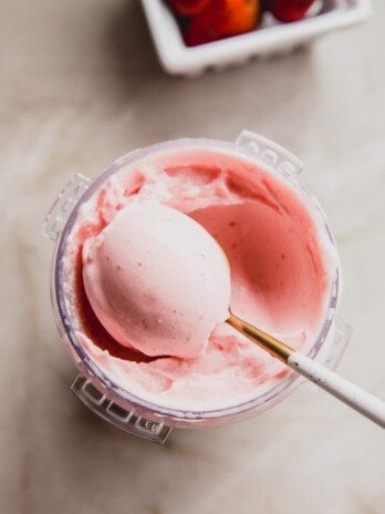 Ninja creami strawberry ice cream with a spoon taking a scoop, and strawberries in the background.