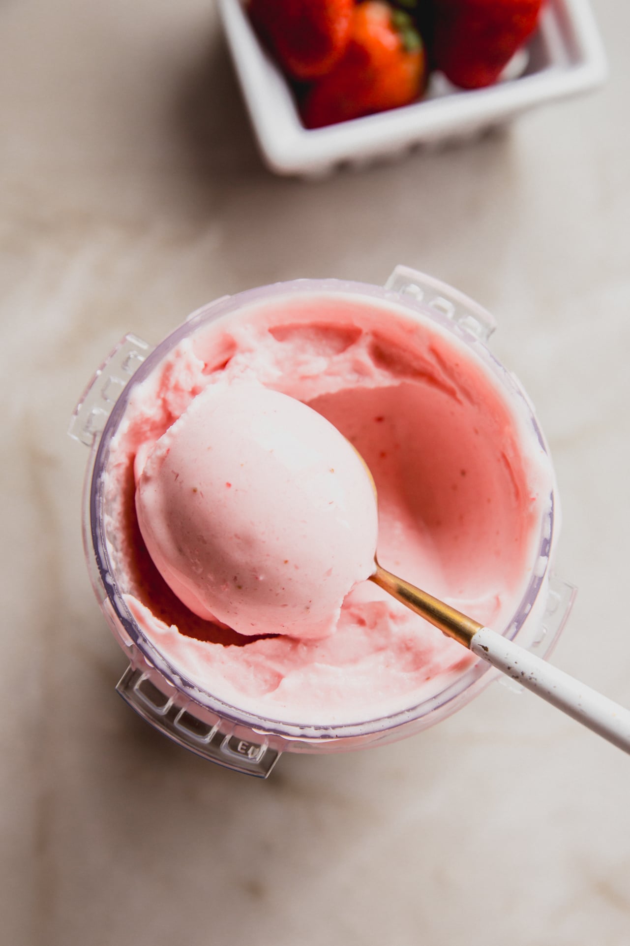 Ninja creami strawberry ice cream with a spoon taking a scoop, and strawberries in the background.