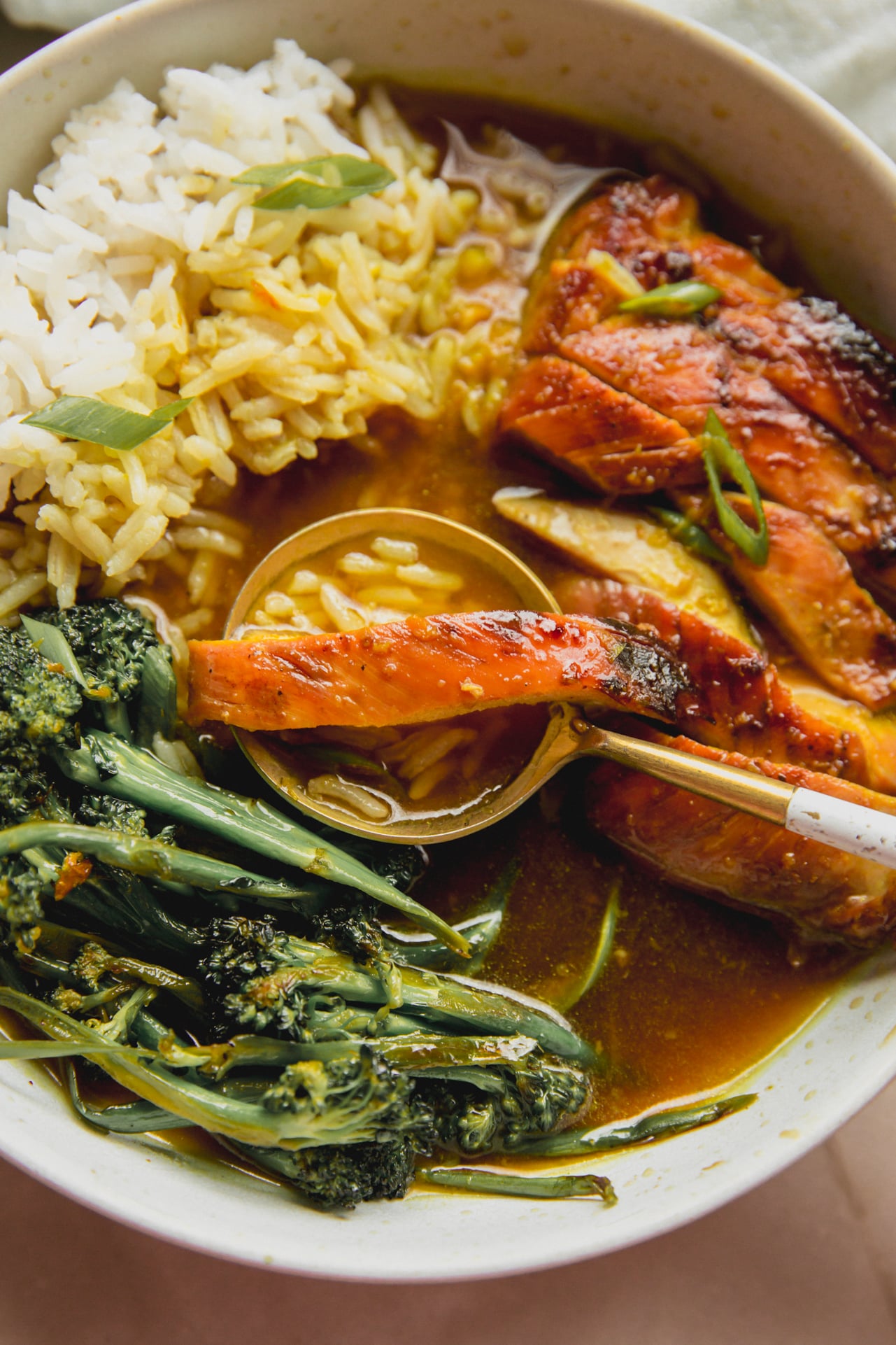 A white bowl with turmeric chicken and rice with a spoon taking a piece of chicken, rice, and broth out.