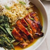 Sliced chicken thighs, broccolini and rice in a bowl with a turmeric broth.