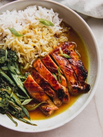 Sliced chicken thighs, broccolini and rice in a bowl with a turmeric broth.