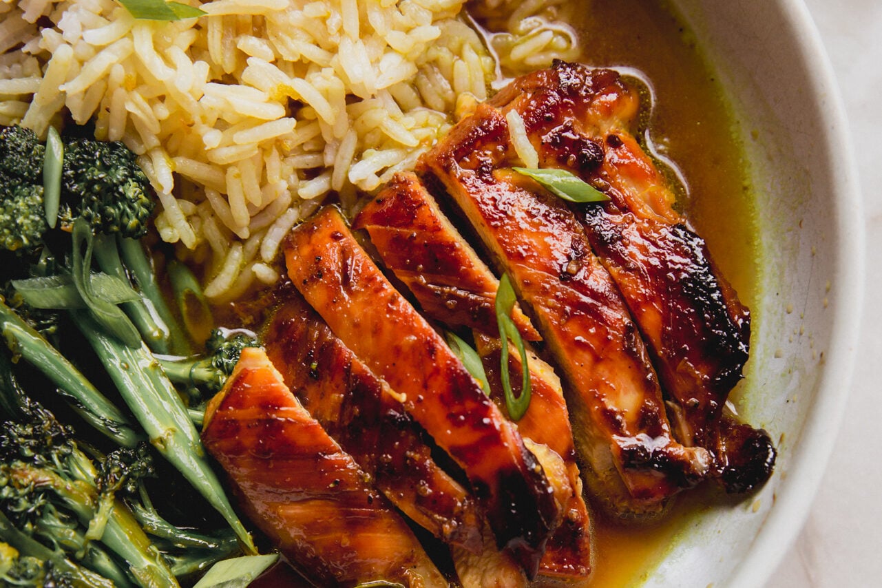 Sliced chicken thighs, broccolini and rice in a bowl with a turmeric broth.