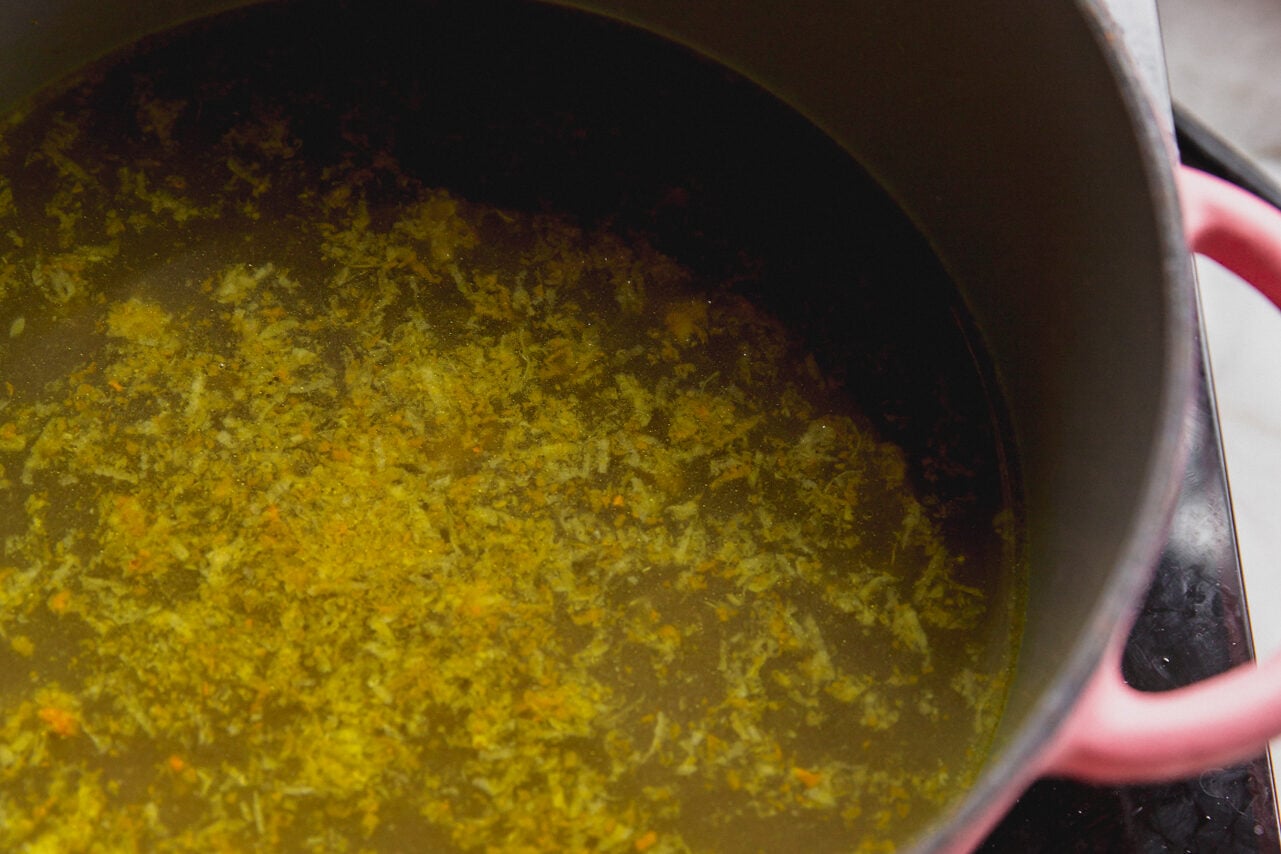 A pink pot with broth cooking in it.