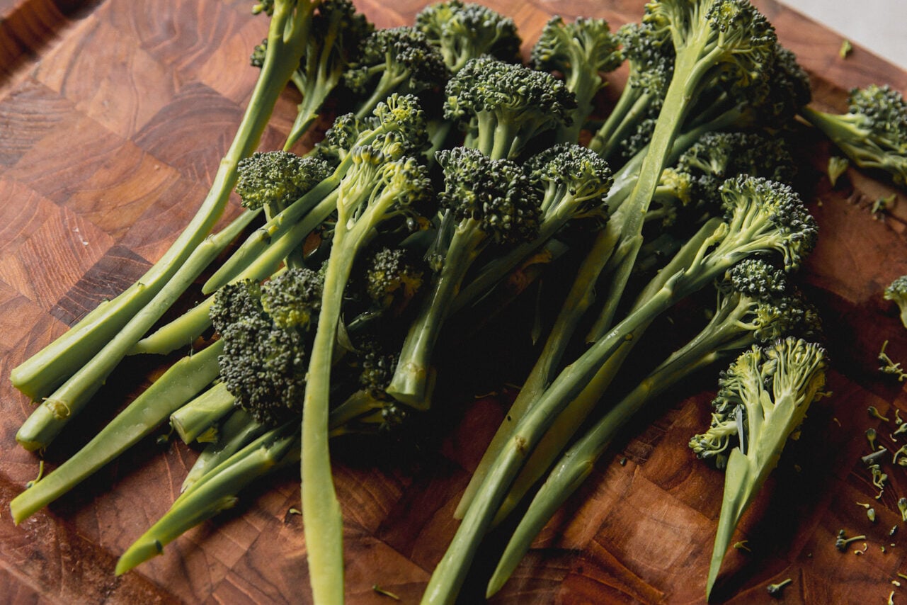 A wooden cutting board with cut broccolini on it before cooking.