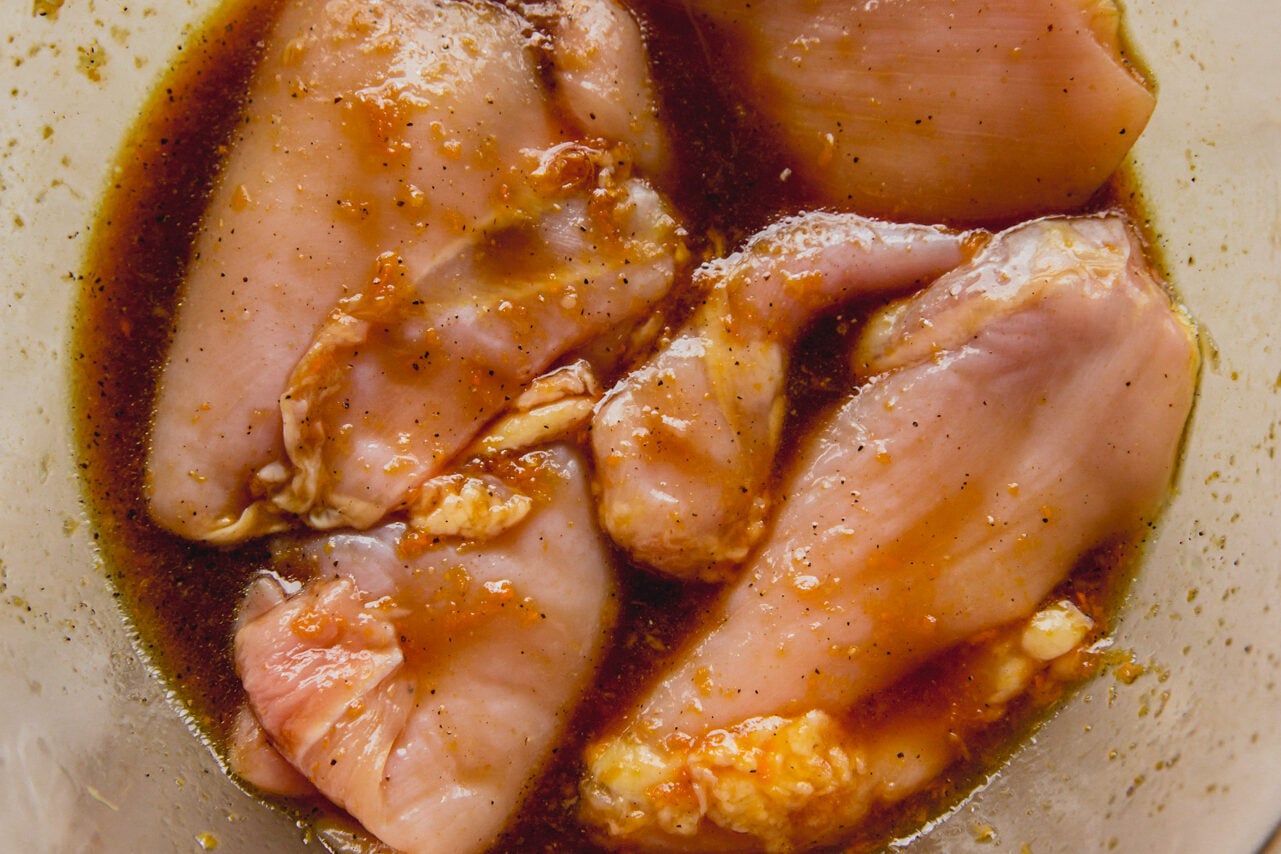 A clear glass bowl with chicken thighs marinating in it.