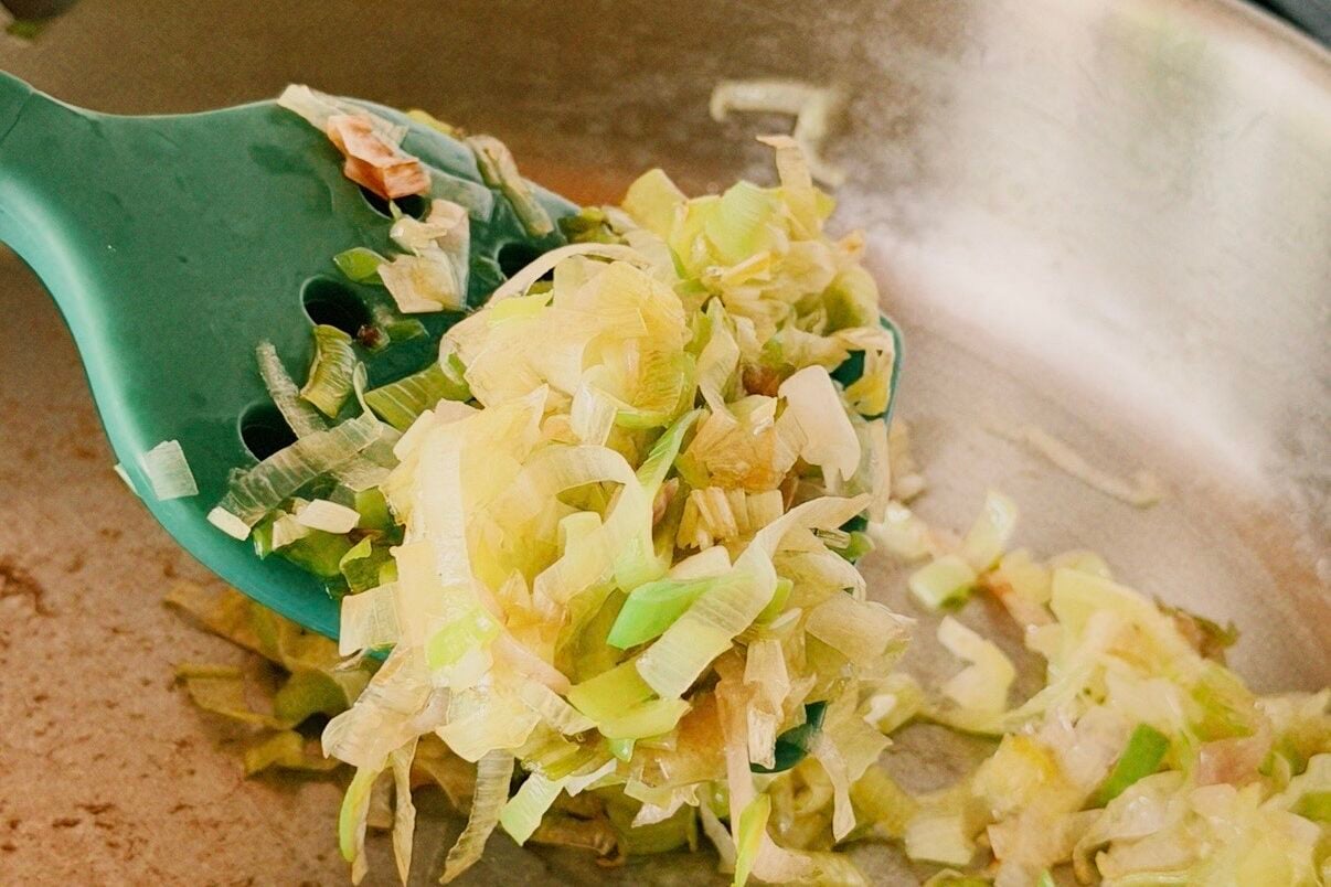 A saute pan with leeks and garlic sauting in it with a green spatula.