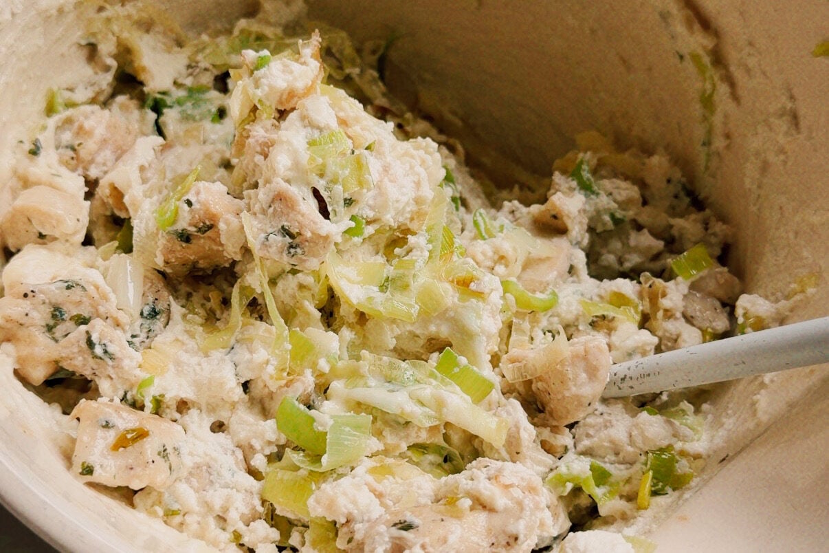 A white ceramic bowl with vegetables and chicken mixed with ricotta to make the shell stuffing mixture.