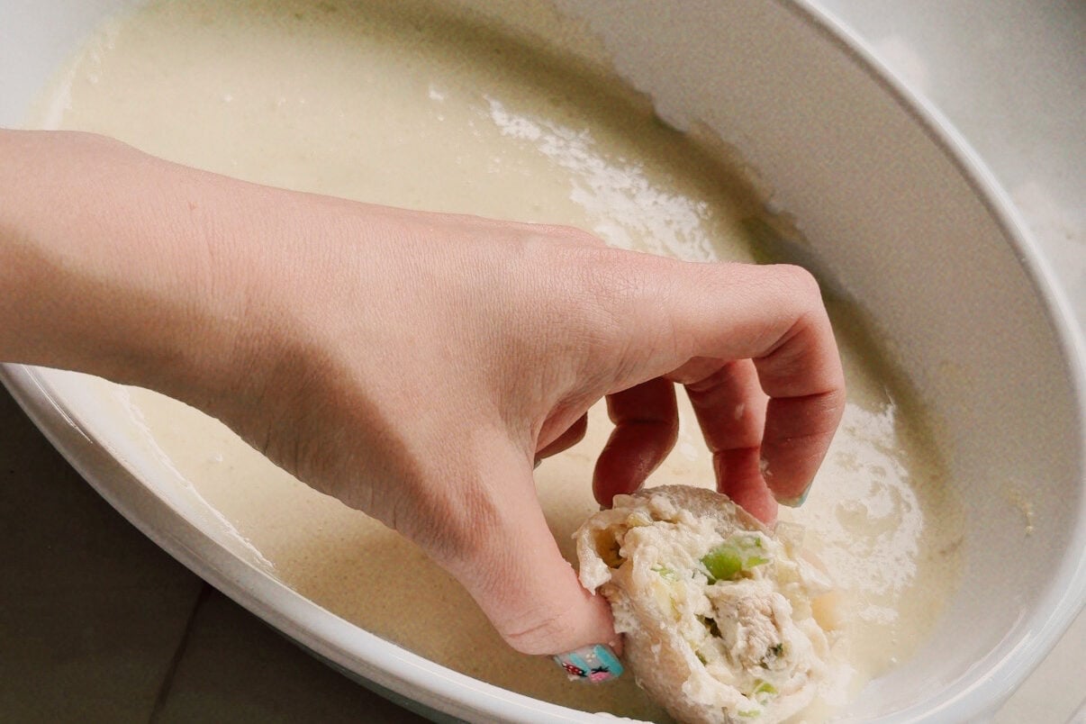 A white ceramic dish with a hand putting a stuffed shell in it.
