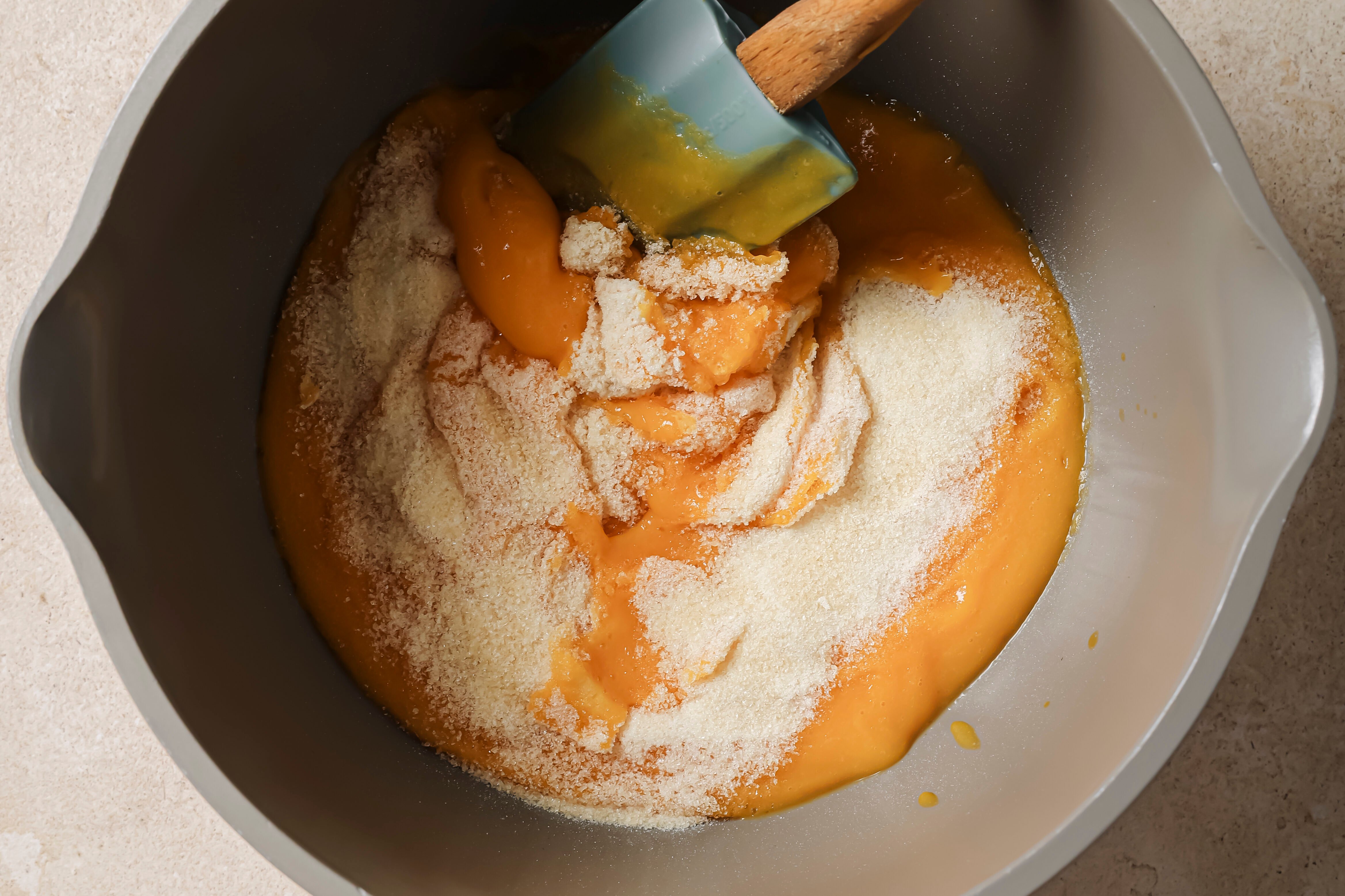 A pot with gelatin sprinkled over the fruit and vegetable mixture with a spatula stirring it.