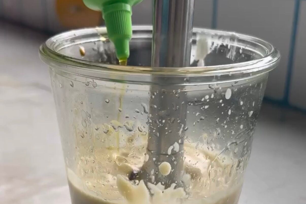 Olive oil streaming in a jar of salad dressing with an immersion blender.