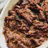Mediterranean pot roast shredded in a large white baking dish.