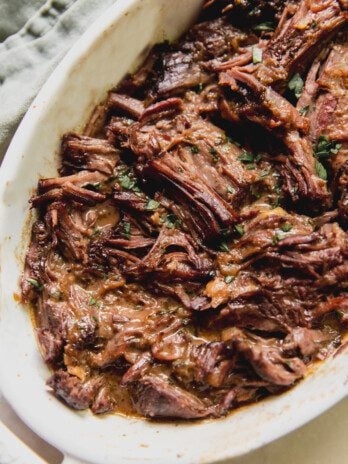 Mediterranean pot roast shredded in a large white baking dish.