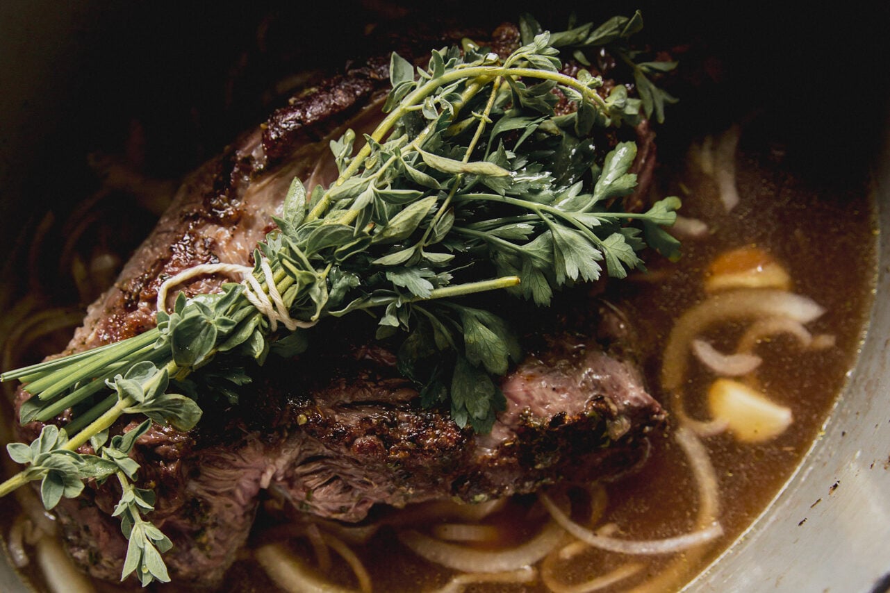 The chuck roast cooking with vinegar and onions topped with herb bunch before going in the oven.