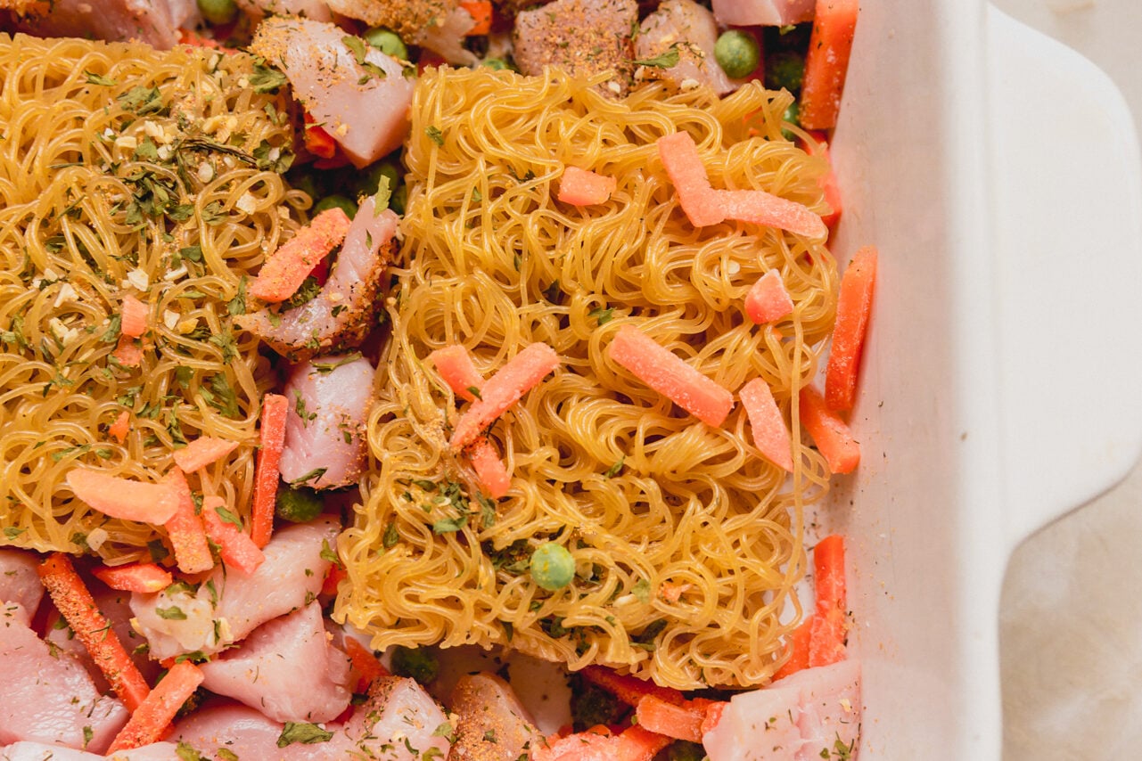 A casserole dish with ramen bricks, vegetables, and chicken in it before liquid is added.