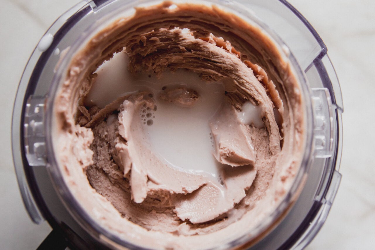 The creami container after one mixing with a well in the middle with almond milk poured in.