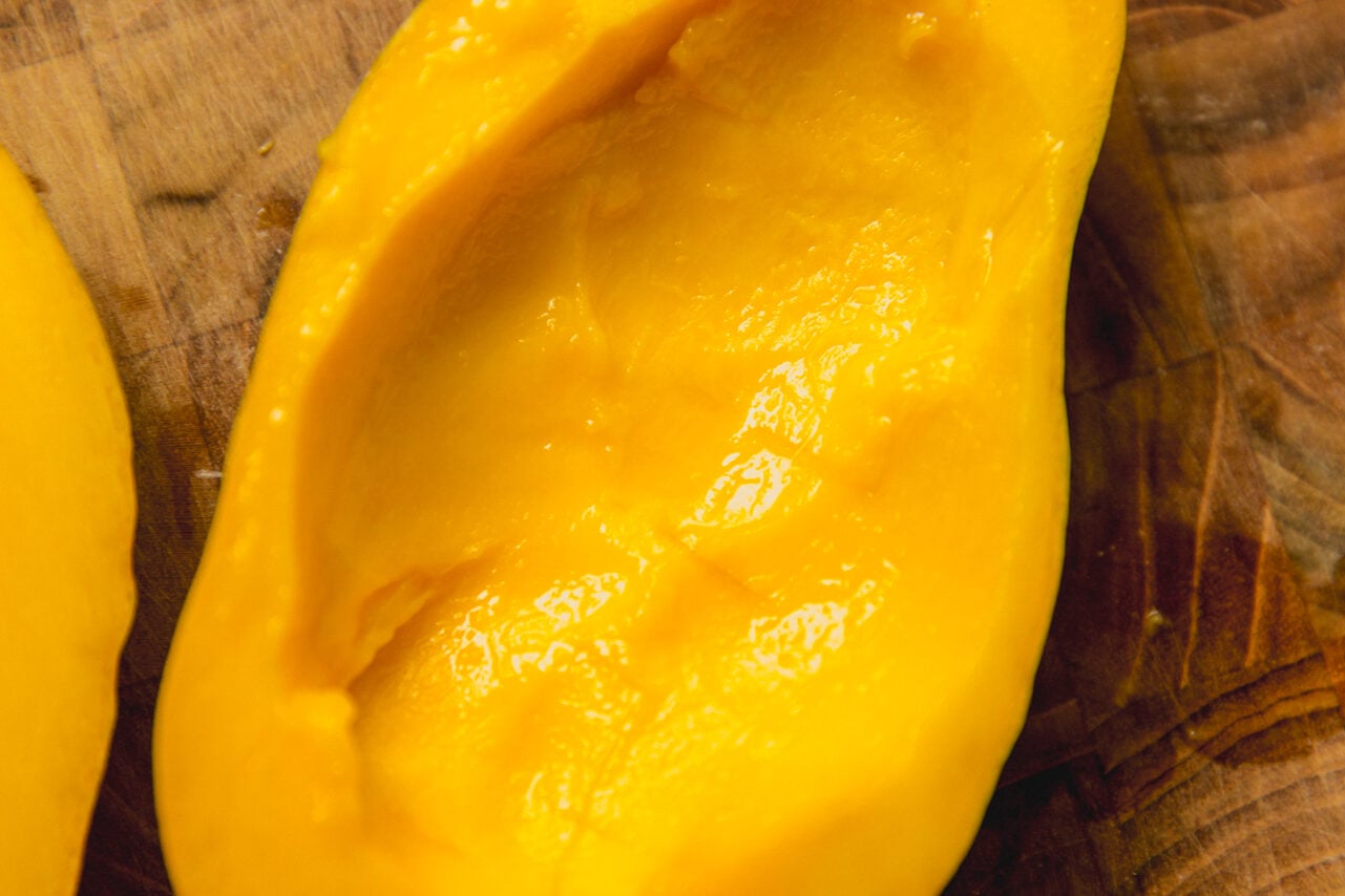 A hallowed out mango half sittign on a wooden cutting board.