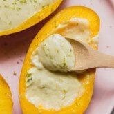Mango posset topped with lime zest, and a wooden spoon dipping the creamy filling.