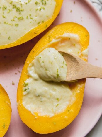 Mango posset topped with lime zest, and a wooden spoon dipping the creamy filling.