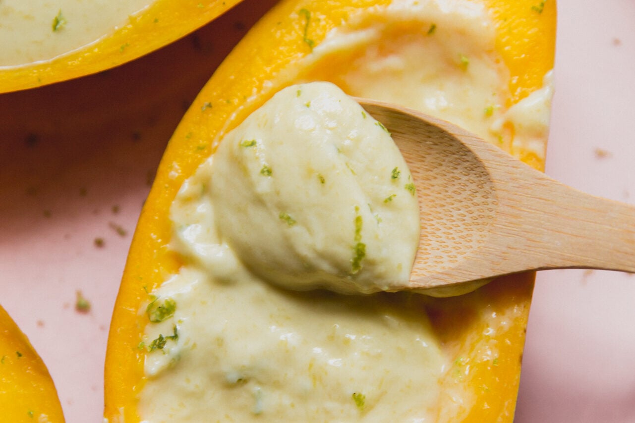 Mango posset topped with lime zest, and a wooden spoon dipping the creamy filling.