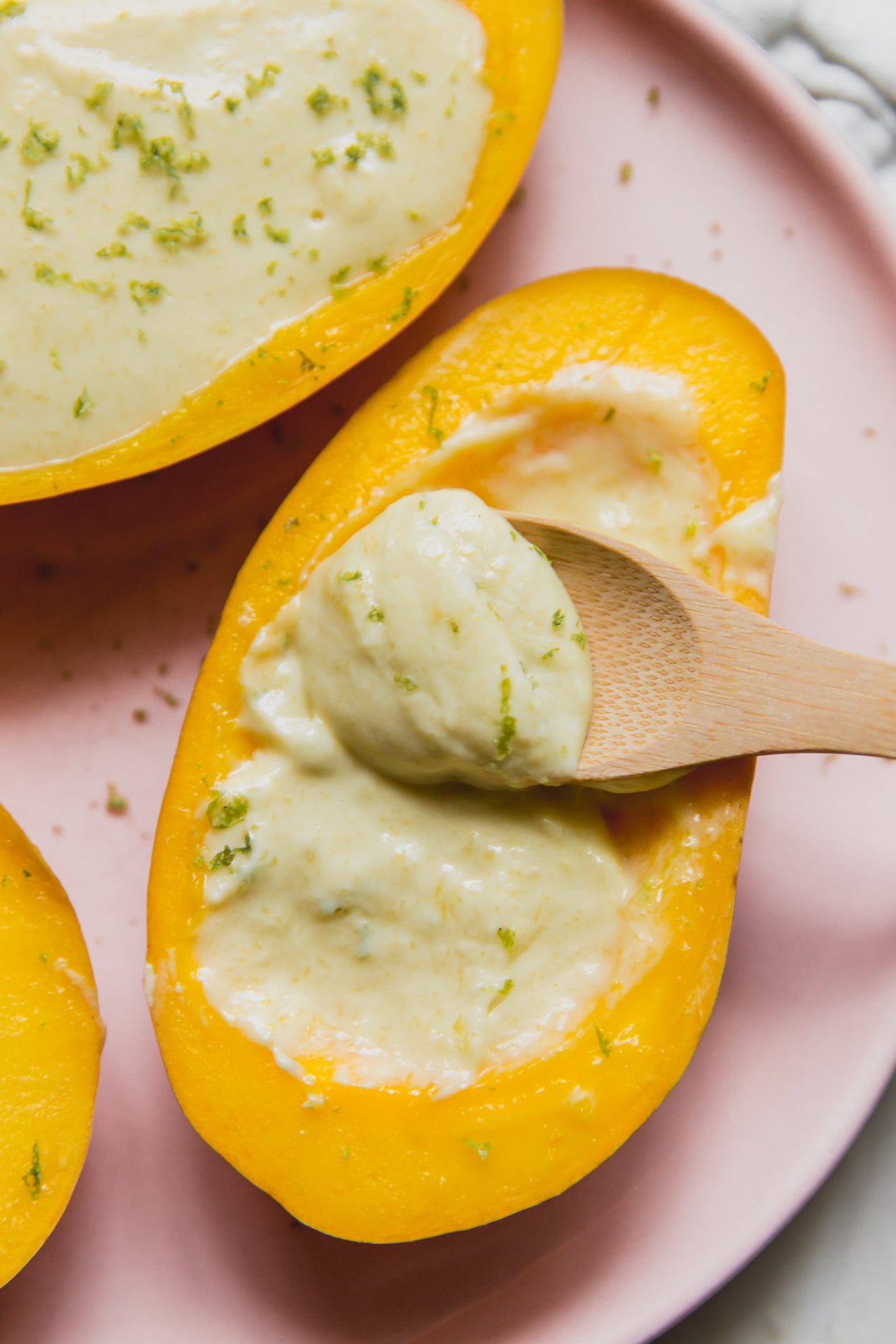 Mango posset topped with lime zest, and a wooden spoon dipping the creamy filling.