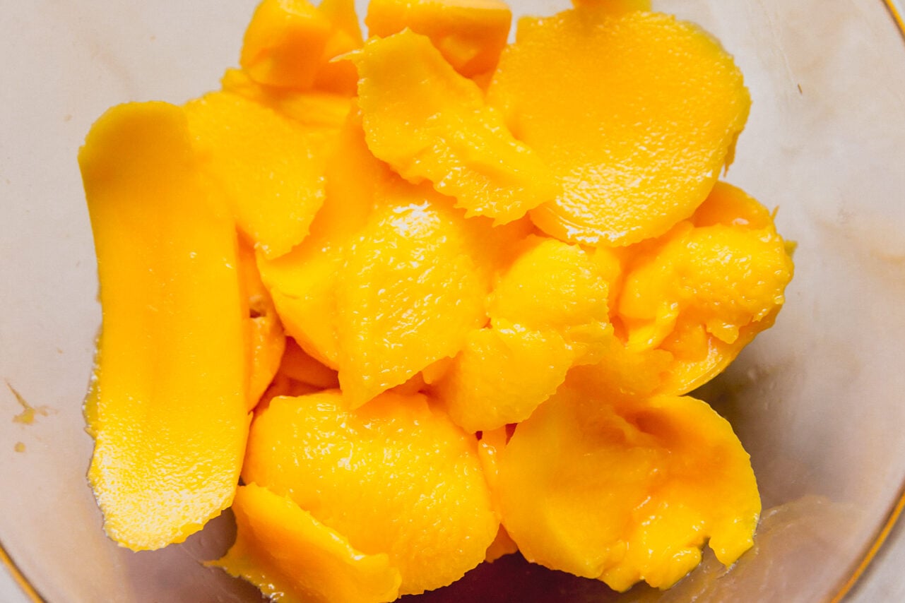 A blender with mango chunks before blending it.