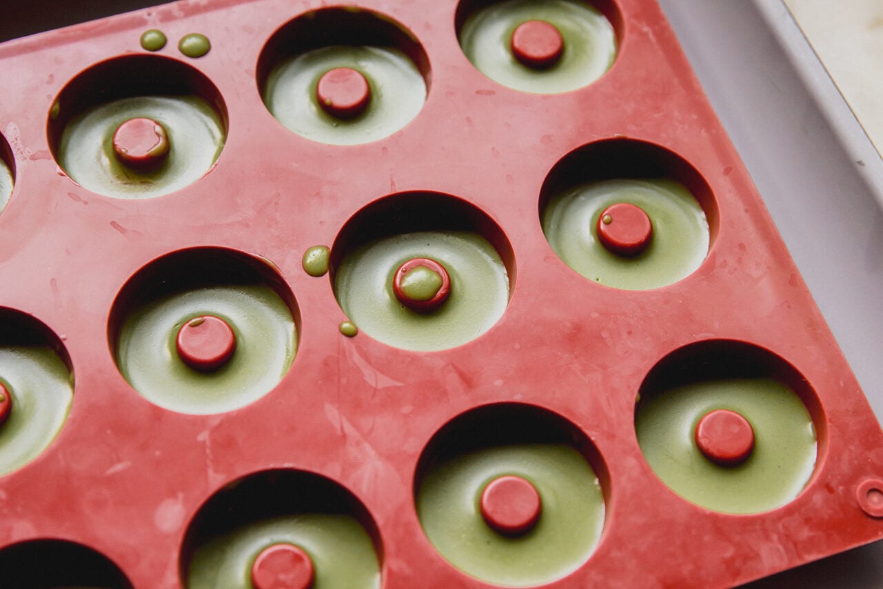A mold filled with the matcha layer on top of the orange mango layer.