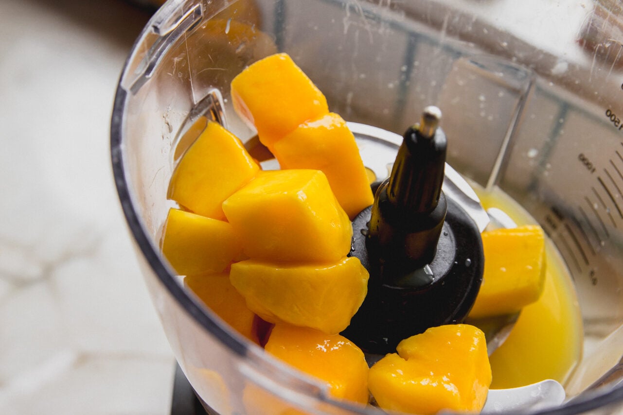 A food processor with mango and orange juice before blending.
