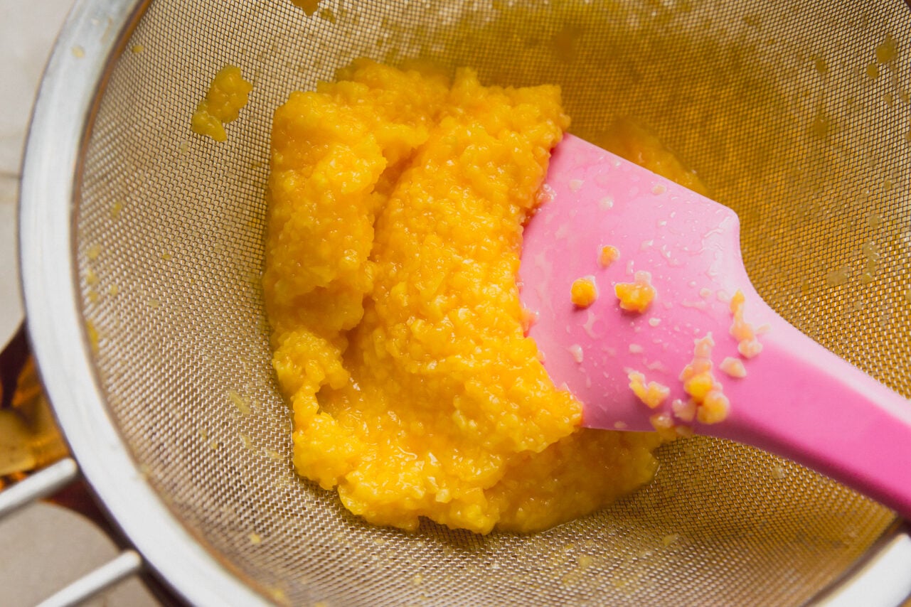 A spatula pushing down the mango orange juice mixture to seperate the pulp and juice.