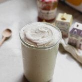 Peach vanilla marshmallow fluff in a tall glass jar with jam and spice jars in the background.