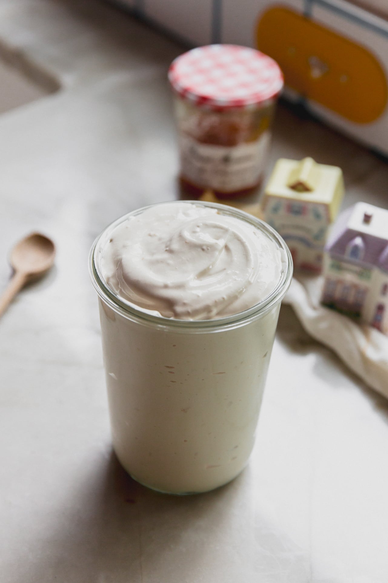 Peach vanilla marshmallow fluff in a tall glass jar with jam and spice jars in the background.