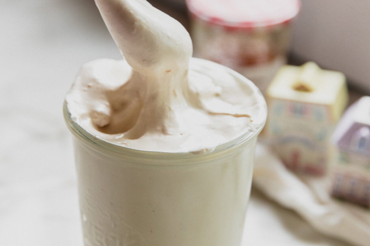 A glass jar filled with peach vanilla marshmallow fluff with a spoon scooping some out.