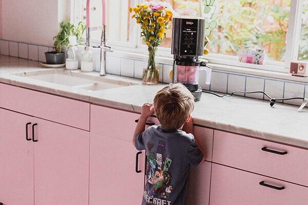Ninja creami blending strawberry pink drink sorbet on a counter in a pink kitchen.