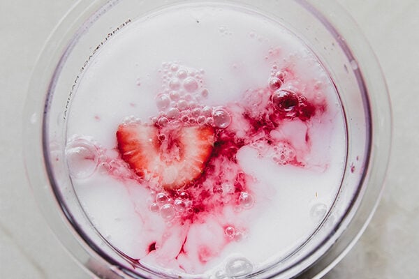 Strawberries, coconut milk and juice in a ninja creami container, ready to be frozen.