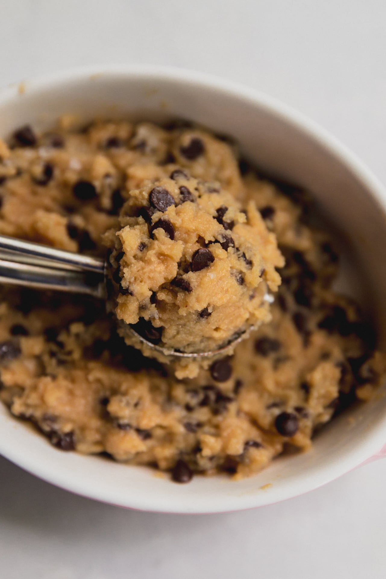 A white bowl of protein cookie dough with a metal scoop in it.