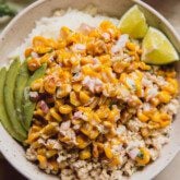 A bowl of rice and ground chicken topped with street corn, avocado and lime.