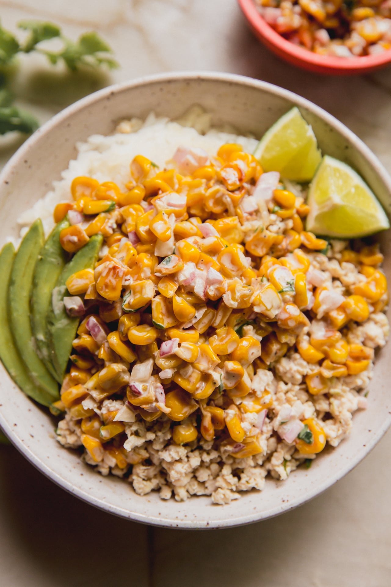 A bowl of rice and ground chicken topped with street corn, avocado and lime.