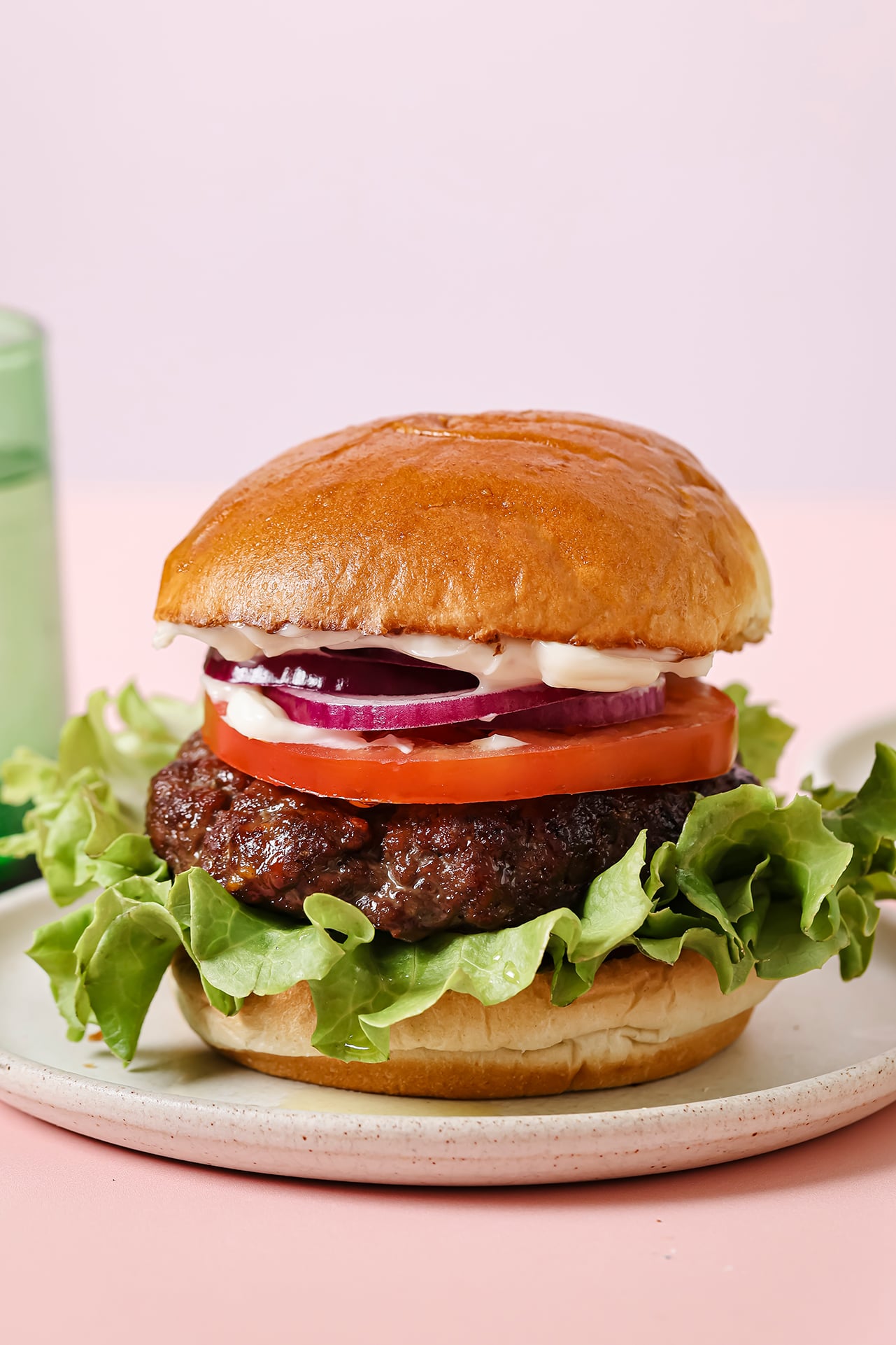 Fully cooked burger with a bun, lettuce and red onion on a white plate.