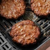Three air fryer burgers fully cooked in the air fryer basket.