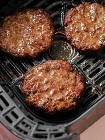 Three air fryer burgers fully cooked in the air fryer basket.